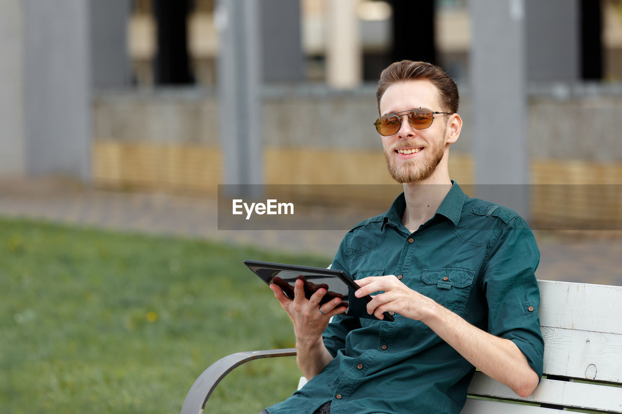 A young man in sunglasses holds a tablet in his hands, reads information on the tablet