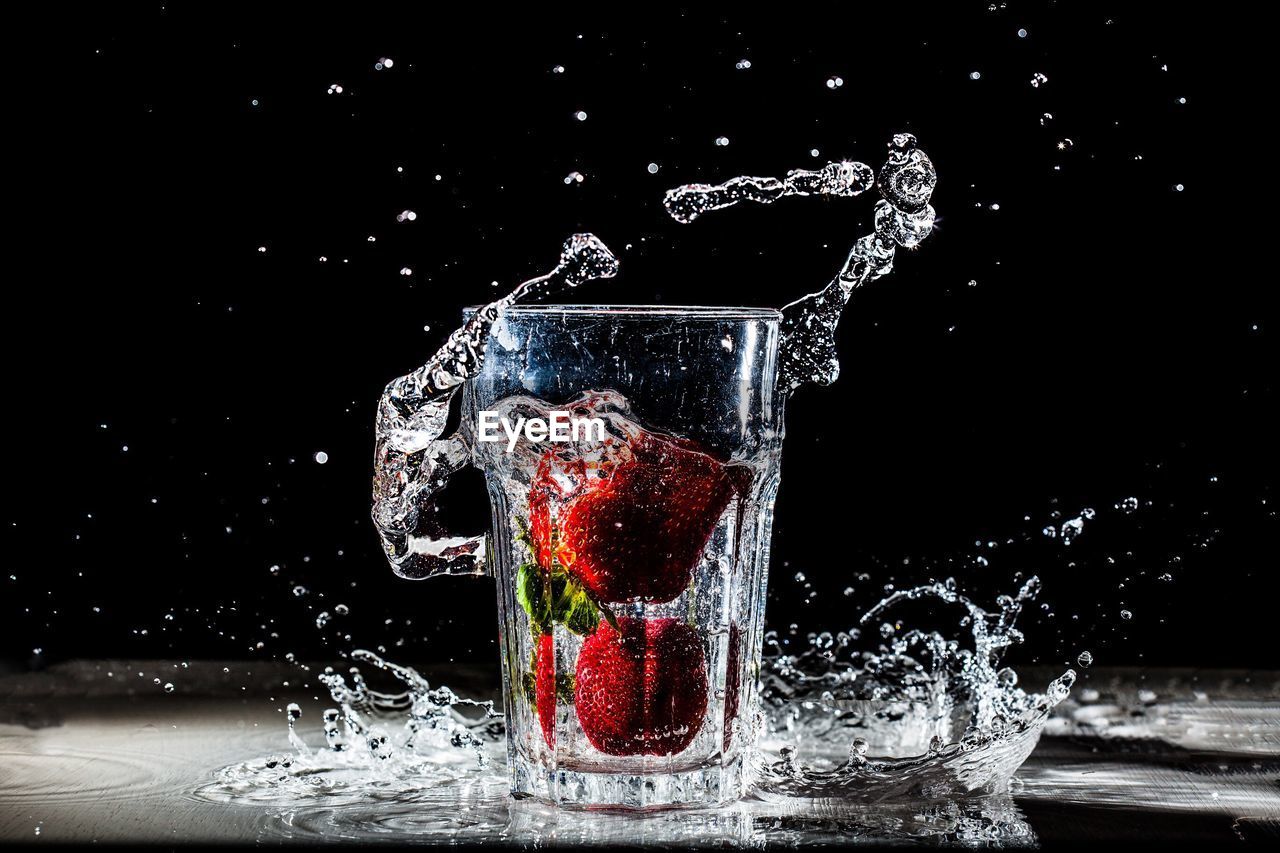 Strawberries splashing in drinking glass filled with water against black background