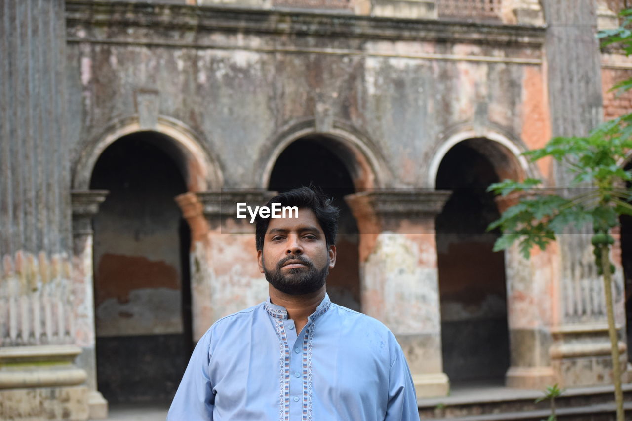 Portrait of bearded man standing against historical building