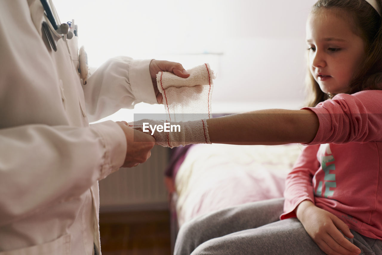 Female doctor bandaging the arm of a little girl in her room. home doctor concept