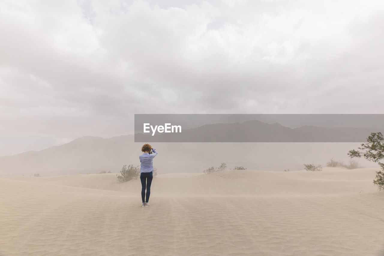 Rear view of woman standing on desert against sky