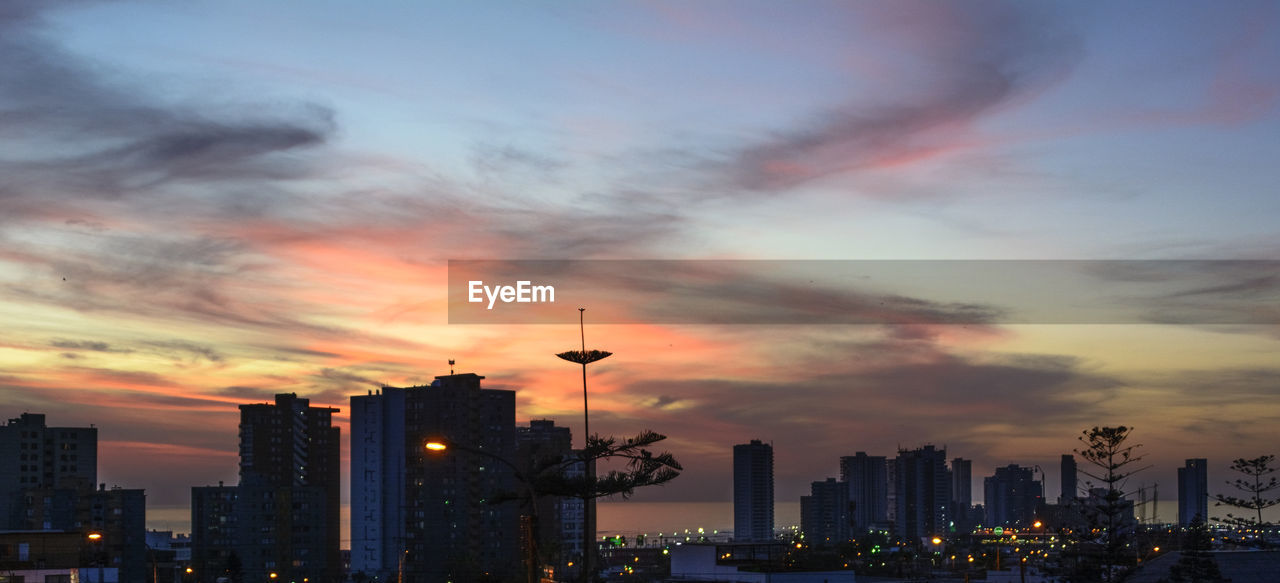 Silhouette of city against cloudy sky during sunset