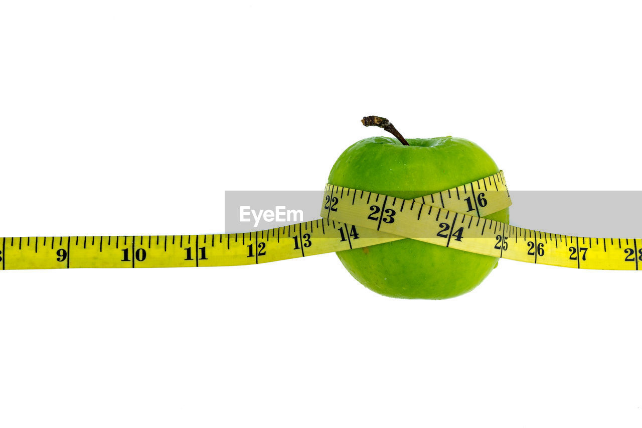 Close-up of apple and tape measure over white background