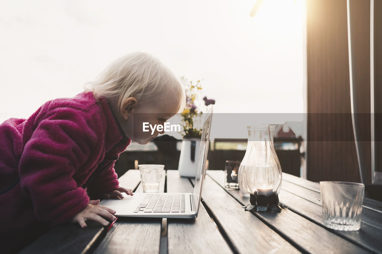 Side view of girl looking at laptop on table in holiday villa against clear sky