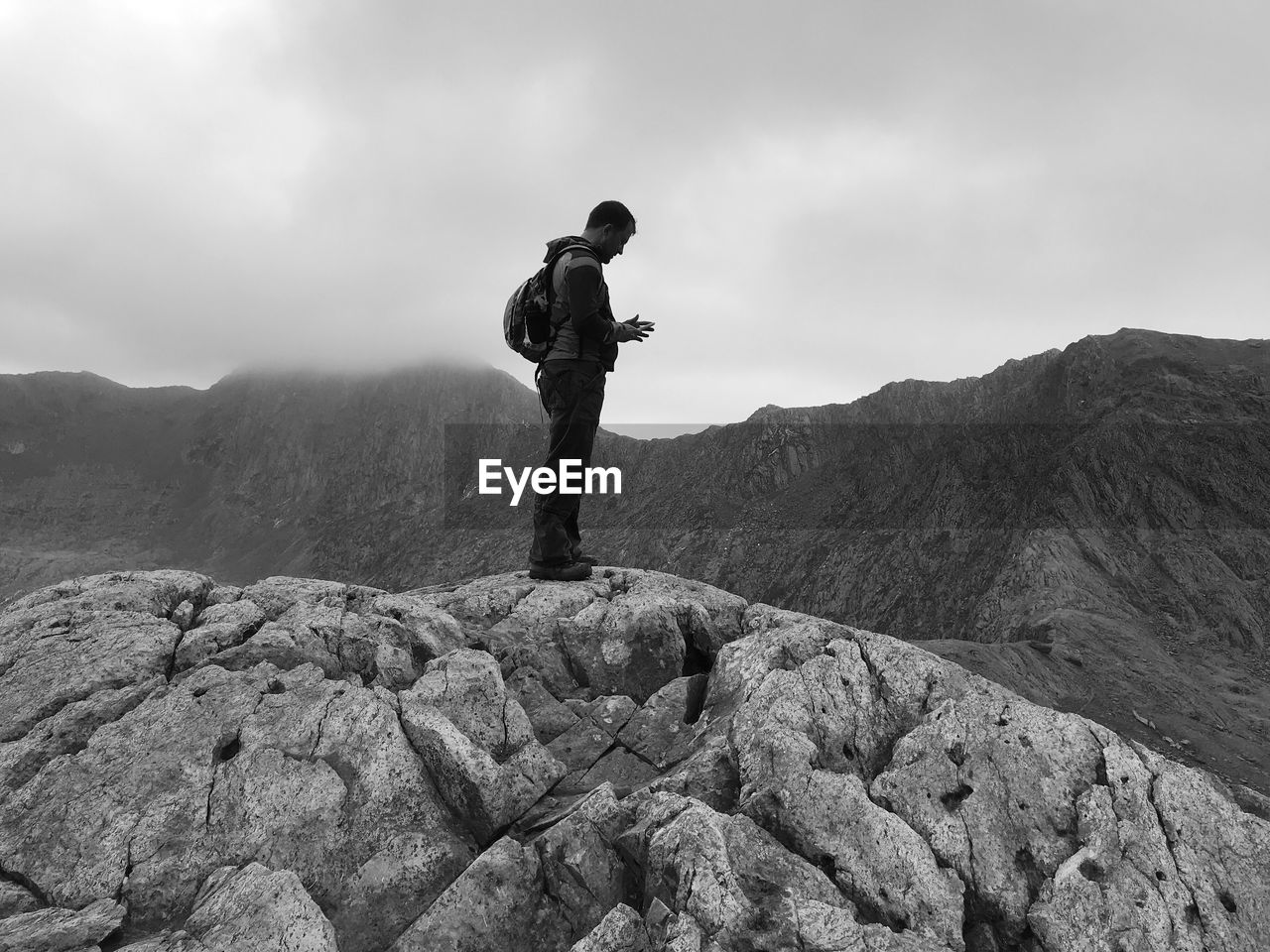 Full length of man using mobile phone while standing on rock against sky