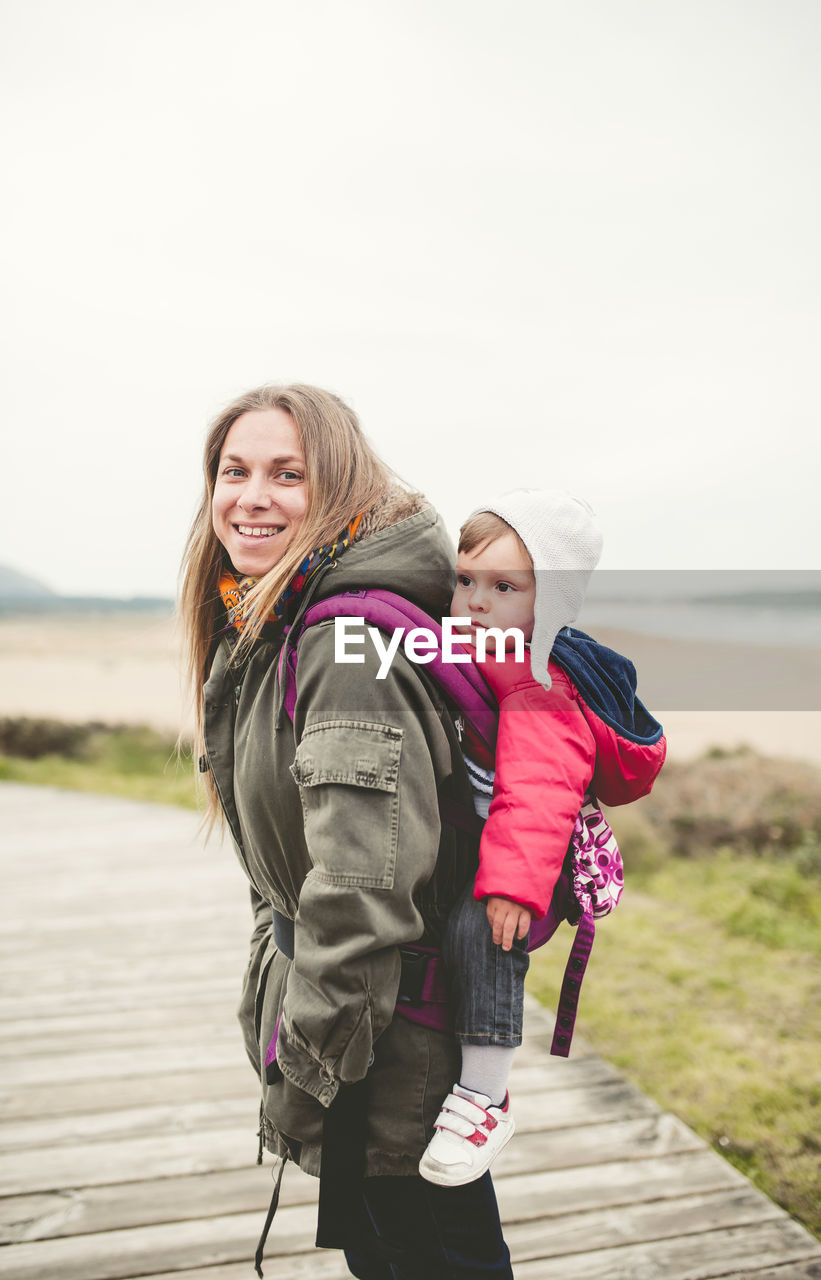 Side view portrait of smiling mother carrying baby boy on boardwalk