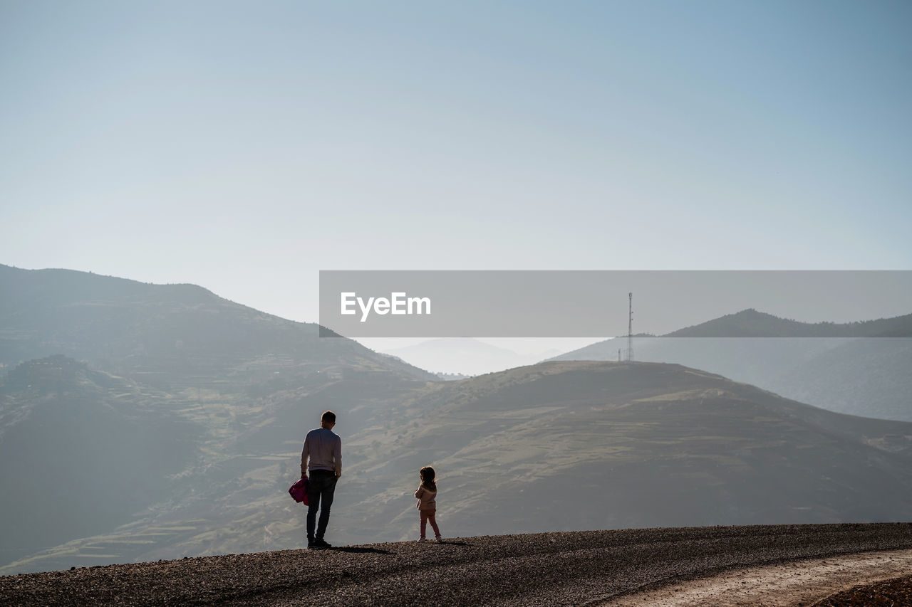 Rear view of father and daughter looking at mountain against clear sky