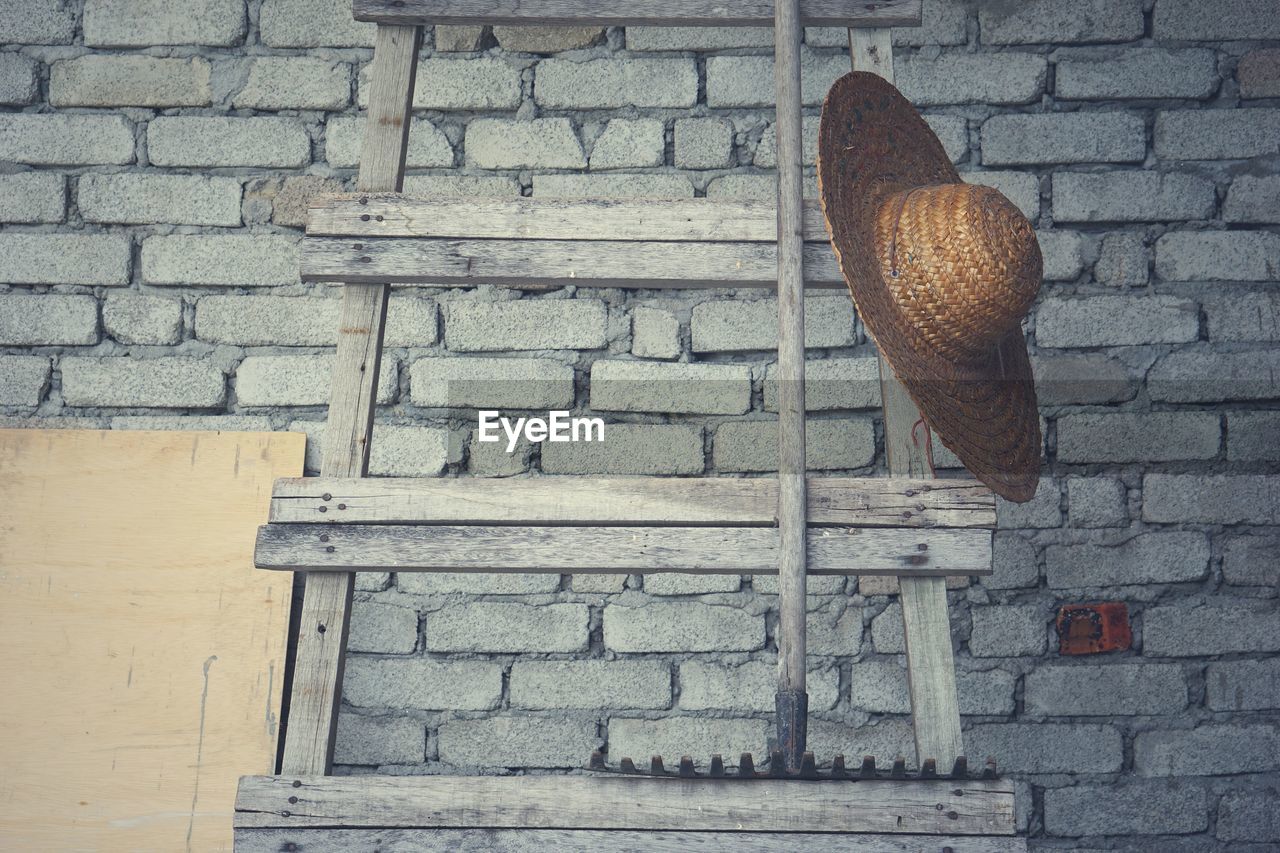 Low angle view of hat hanging on ladder against brick wall