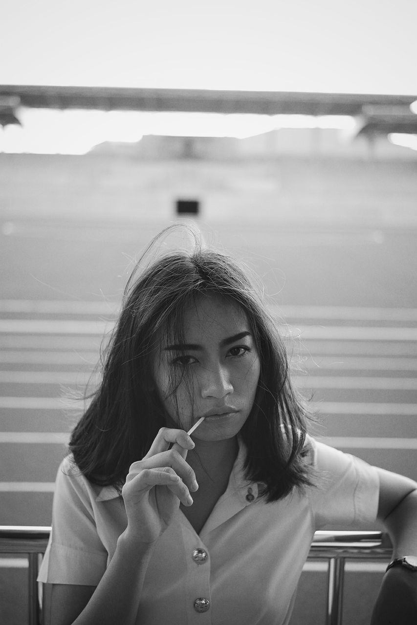 Portrait of beautiful young woman eating lollipop while standing by railing