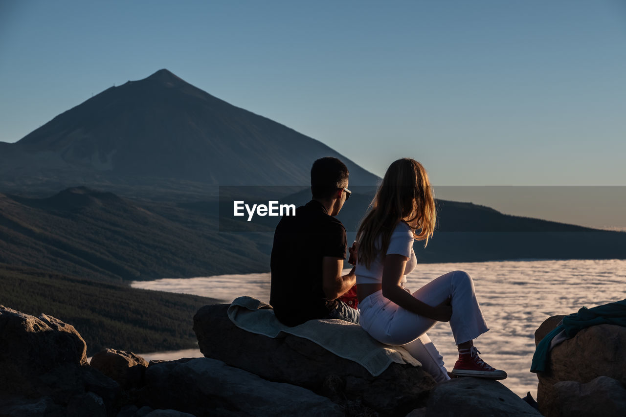 Young couple ist sitting at lookout and watching the sunset with volcano teide in the back.