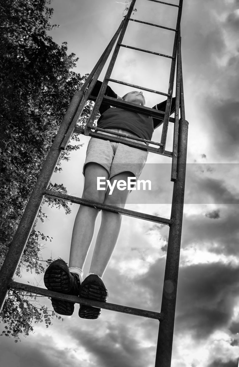 Low angle view of kid on ladder against sky looking up