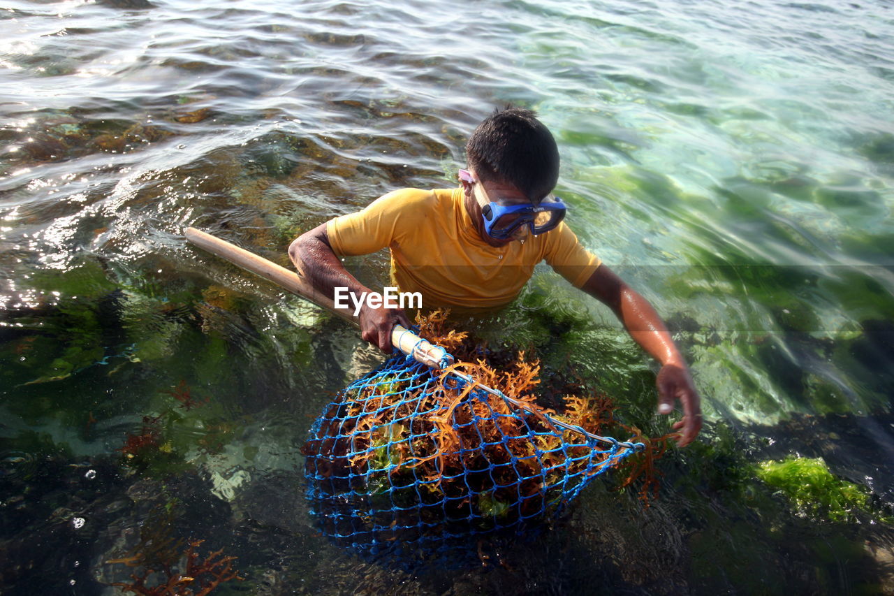 Man holding fishing net with coral in sea