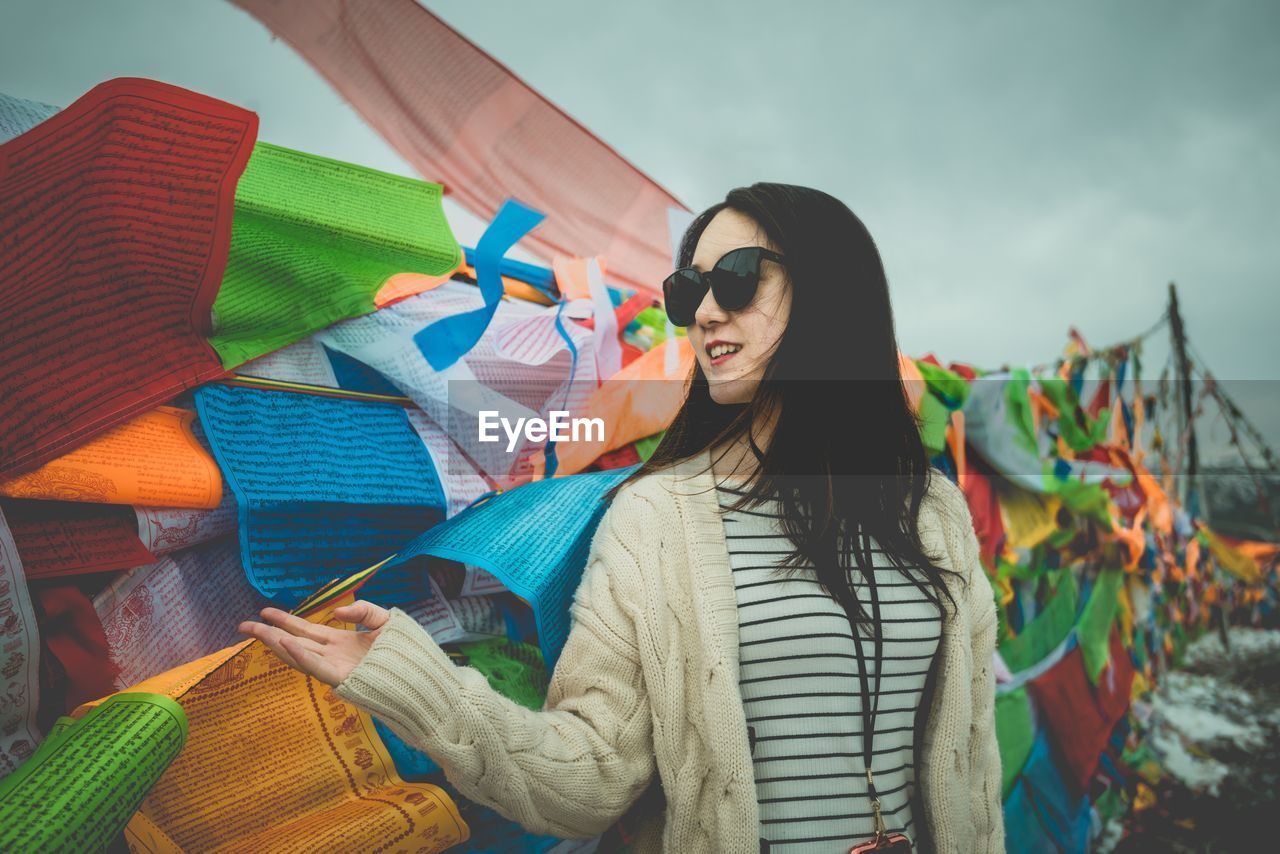 Woman in sunglasses standing against multi colored prayer flags