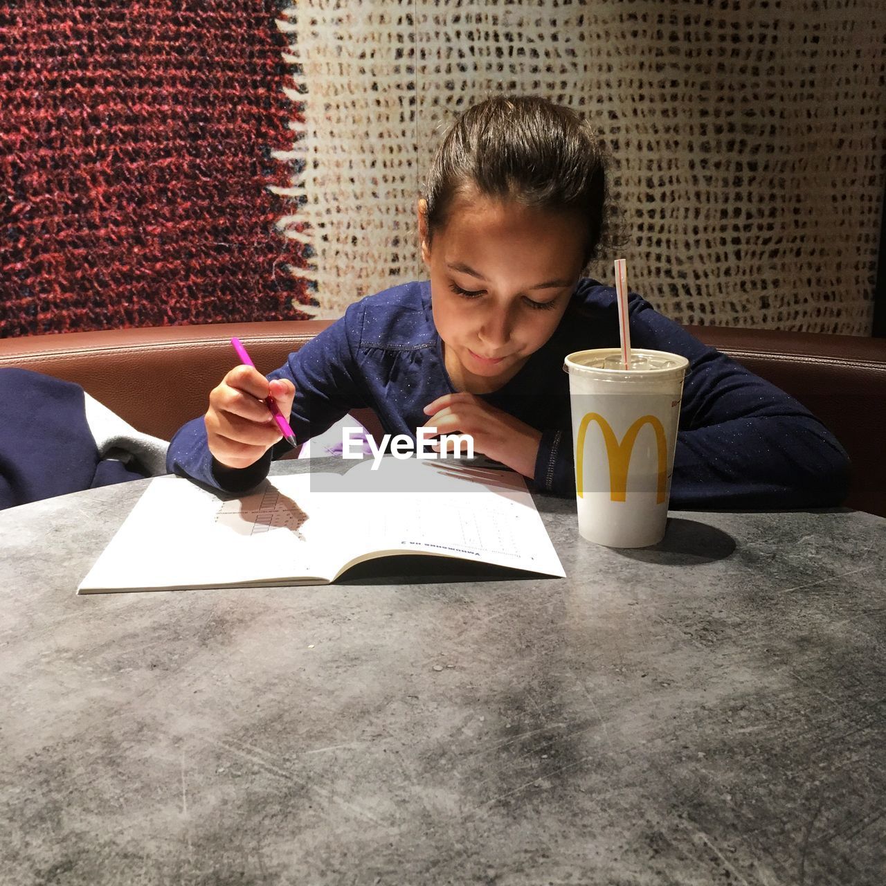 WOMAN SITTING ON TABLE WITH BOOK IN BACKGROUND