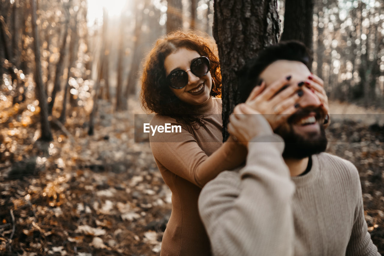 Cheerful woman closing man eyes in forest