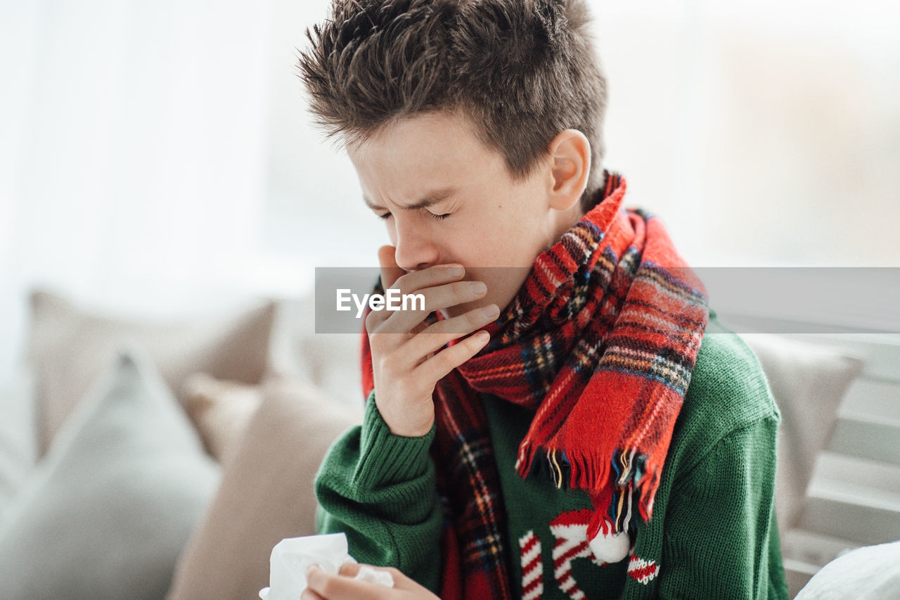 Close-up of boy sneezing at home