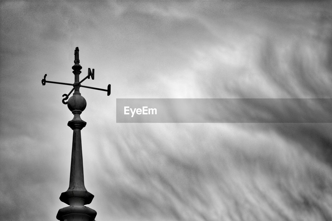 Low angle view of weather vane against cloudy sky