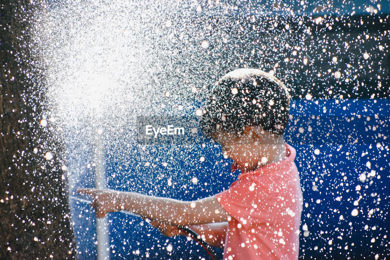 Boy splashing water while holding garden hose