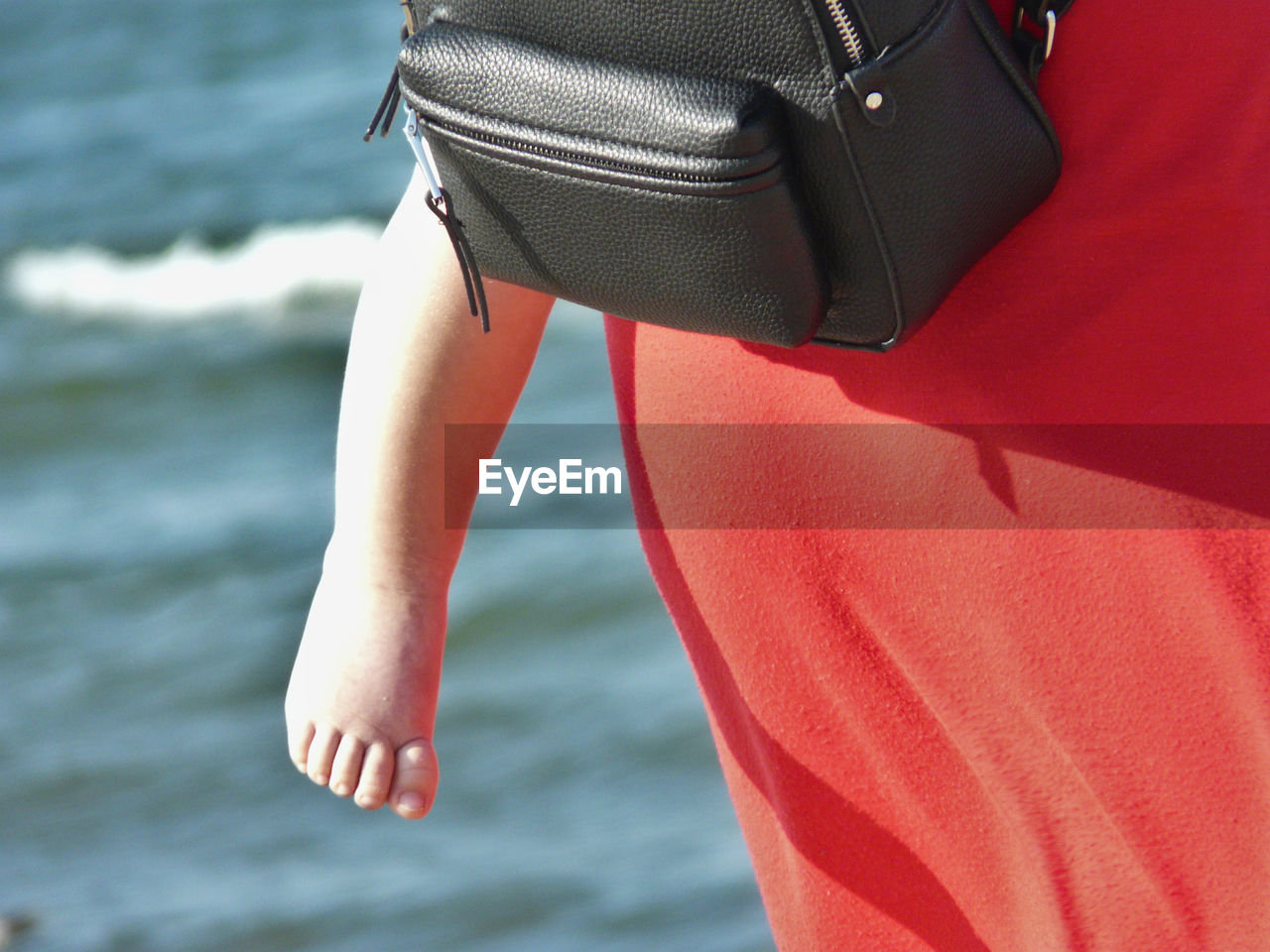 LOW SECTION OF WOMAN WEARING RED SHOES ON SEA