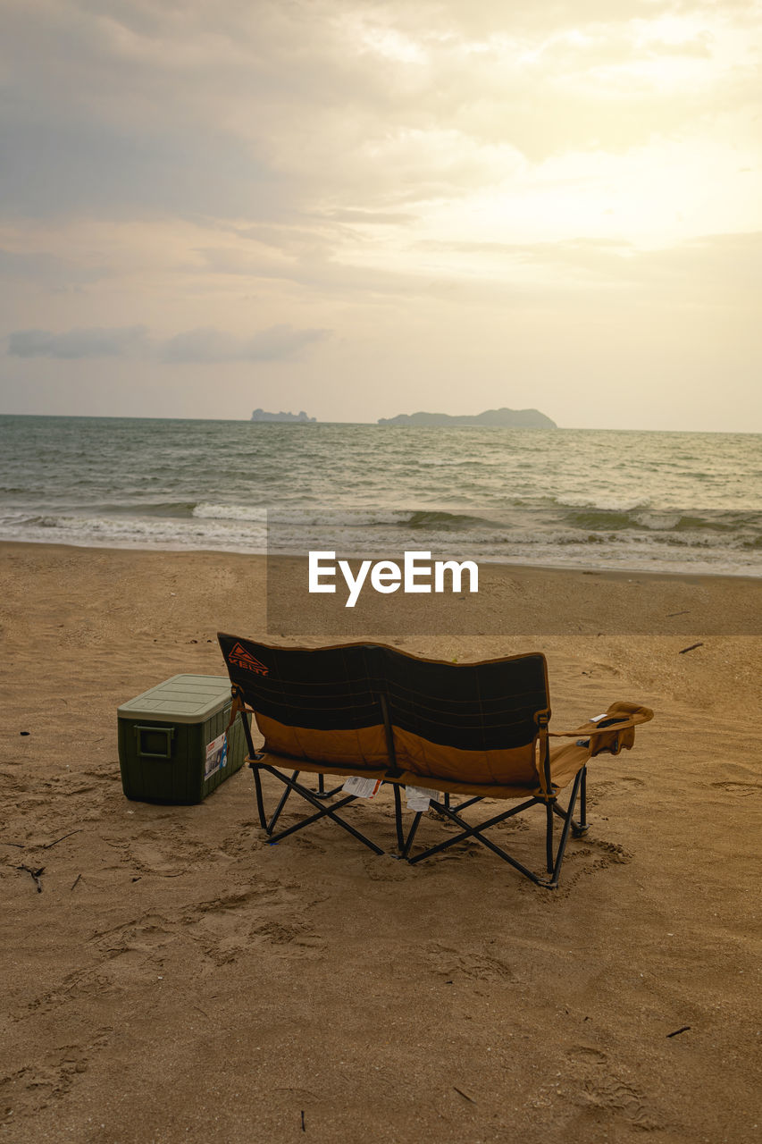 Empty chairs on beach against sky