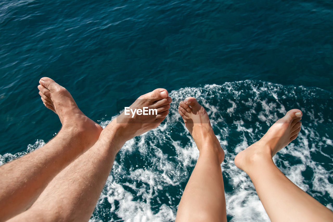 Low section of couple sitting against sea