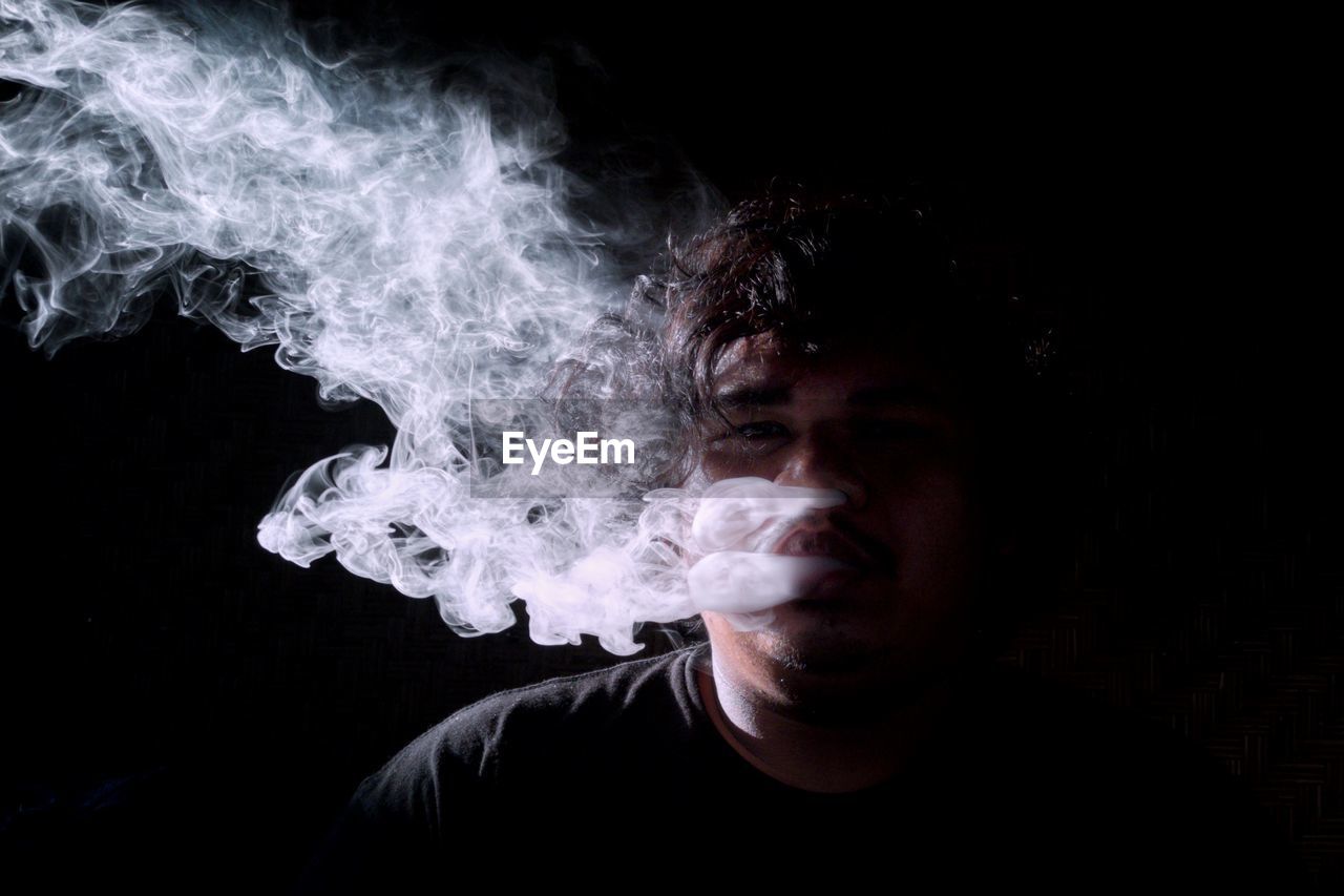 Close-up portrait of man smoking over black background