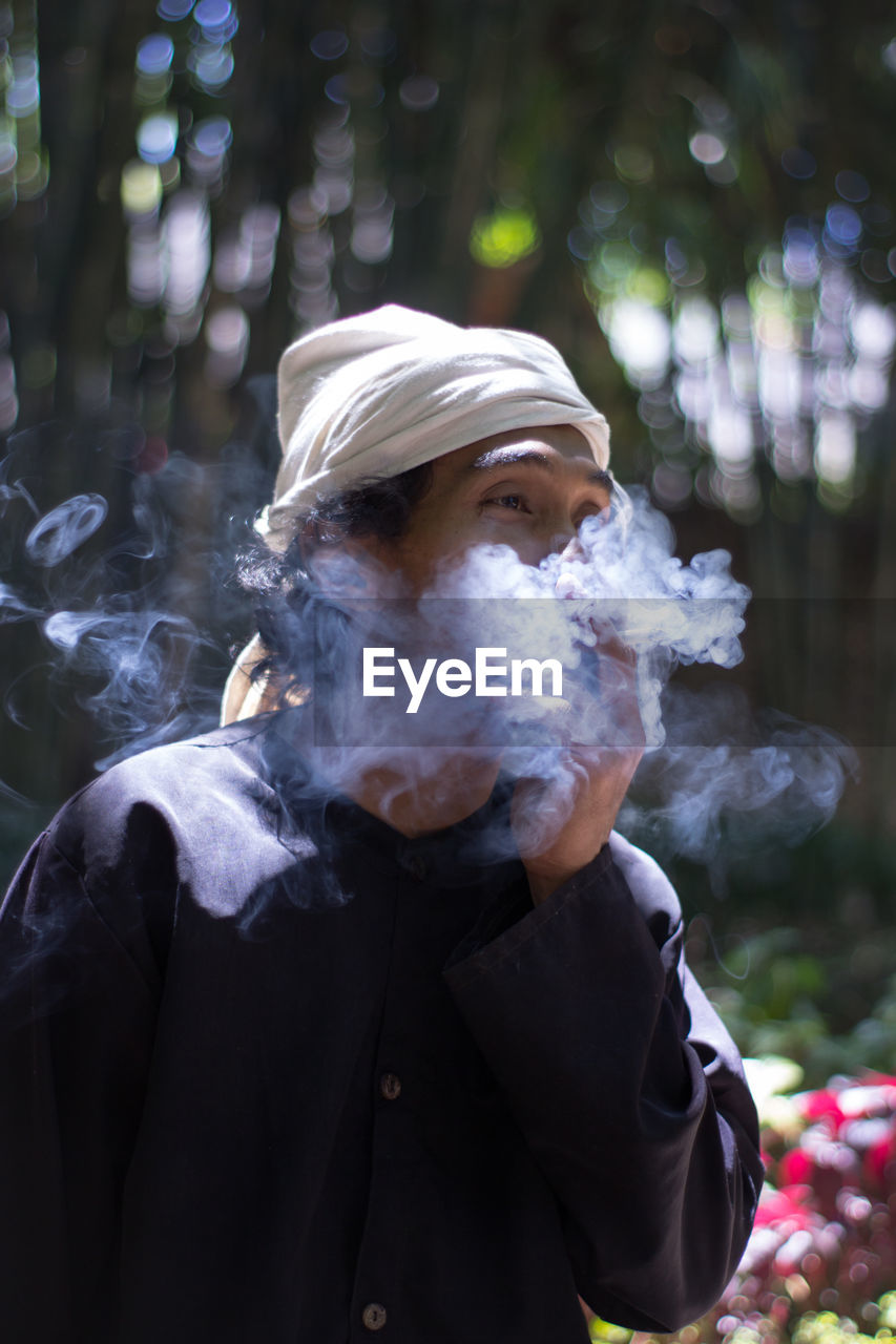 Man smoking while standing against trees