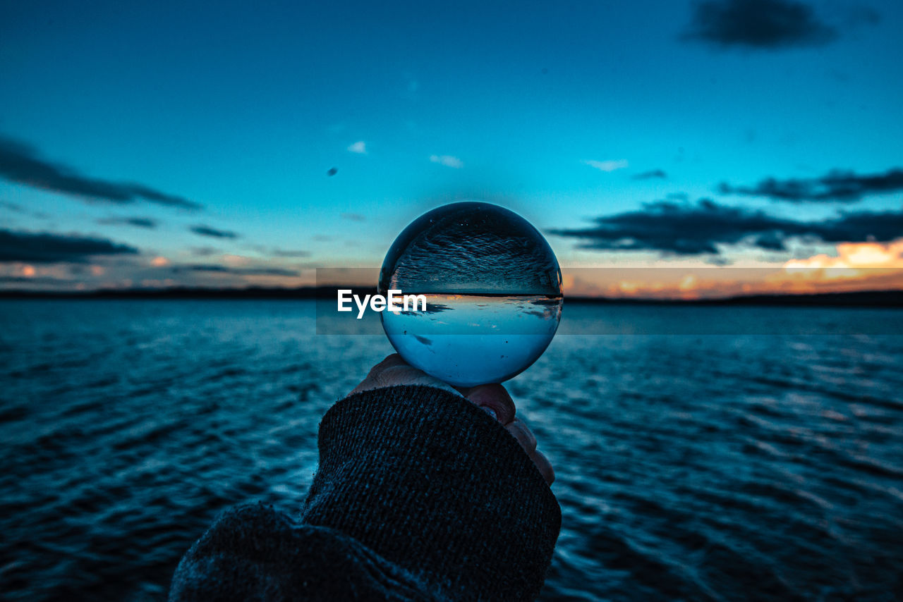 CLOSE-UP OF SUNGLASSES ON SEA AGAINST SKY DURING SUNSET