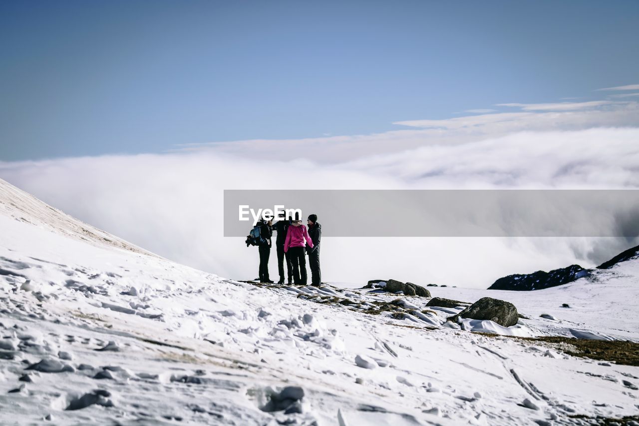 REAR VIEW OF PEOPLE WALKING ON SNOWCAPPED MOUNTAINS AGAINST SKY