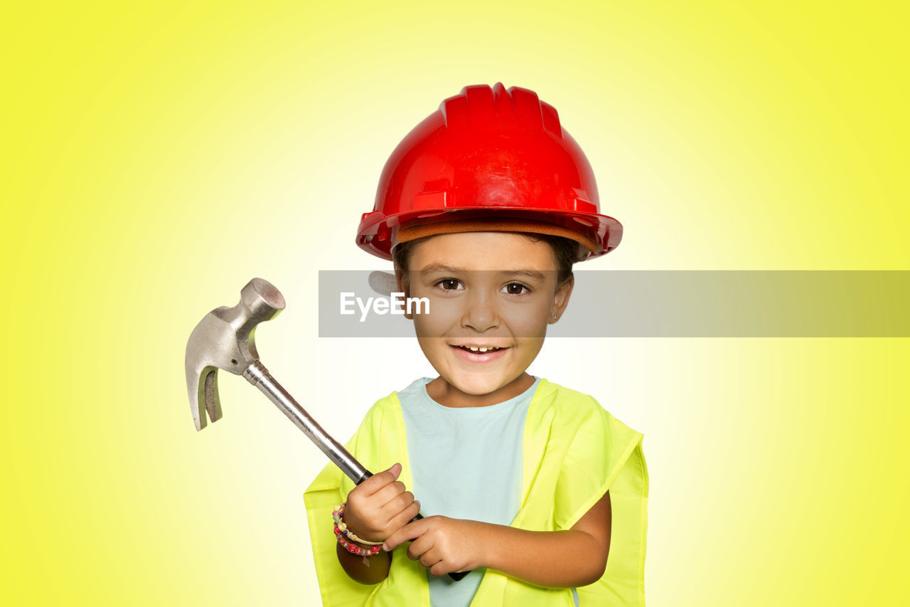 Portrait of smiling cute girl holding claw hammer while standing against yellow background