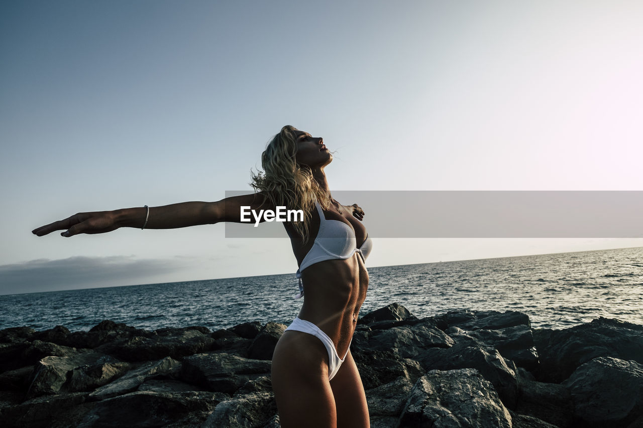 Woman standing on rock by sea against sky