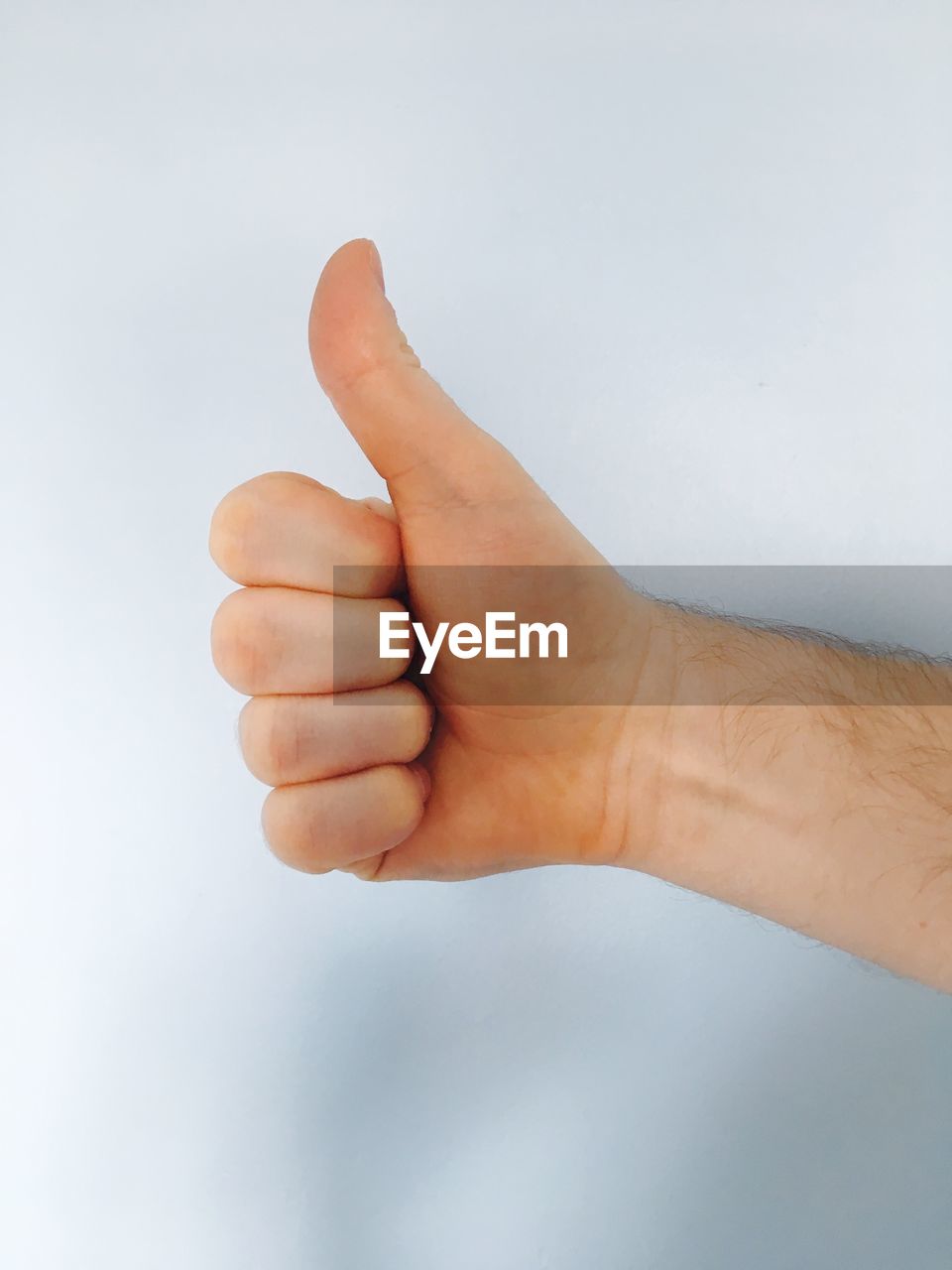 Close-up of hand showing thumbs up against white background