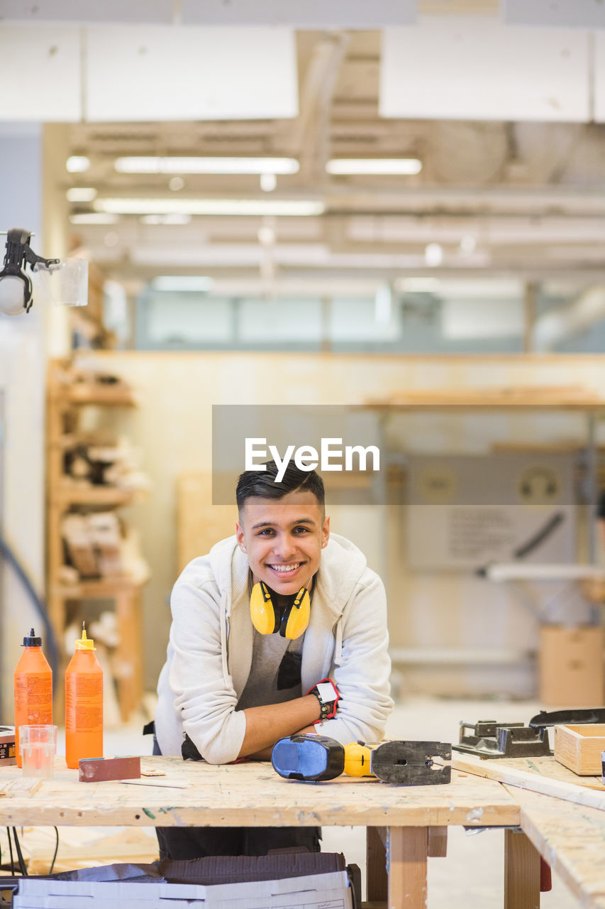 Portrait of smiling teenage trainee leaning on workbench at workshop