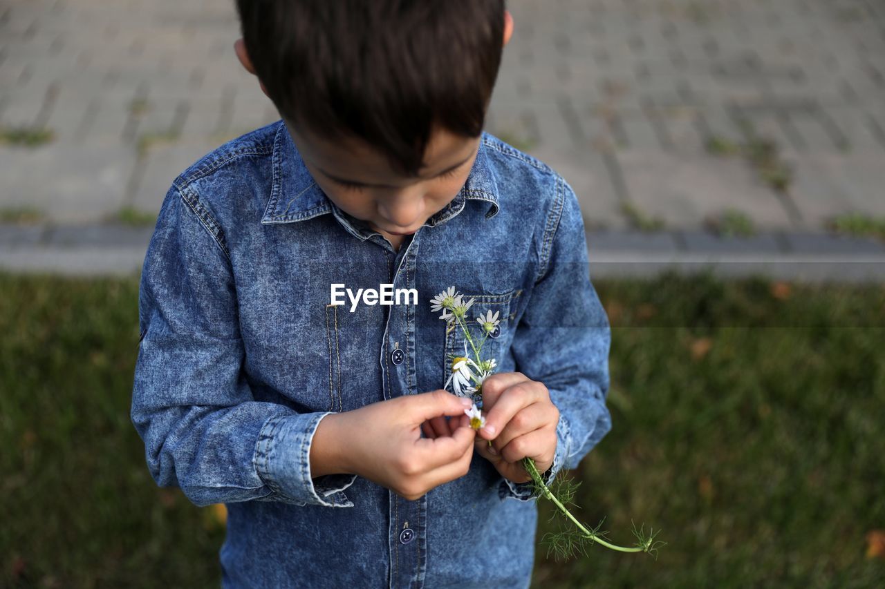 Boy holding flower while standing outdoors