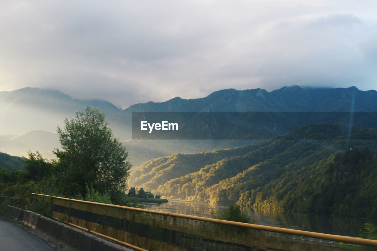 Scenic view of mountains by river against cloudy sky