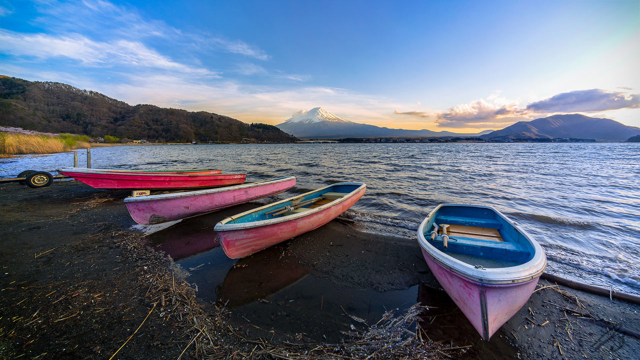 BOATS MOORED ON SHORE BY LAKE AGAINST SKY