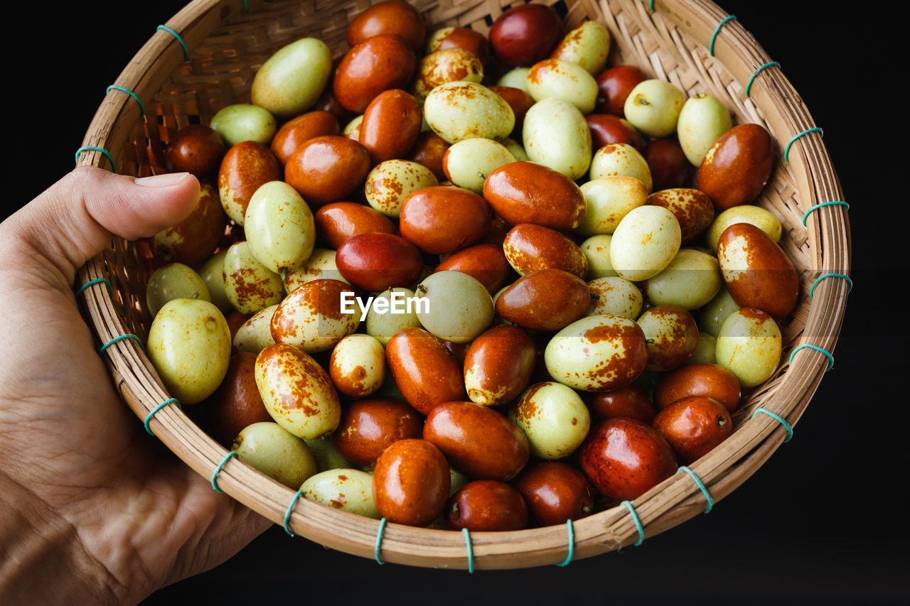 Cropped hand holding fruits in basket against black background