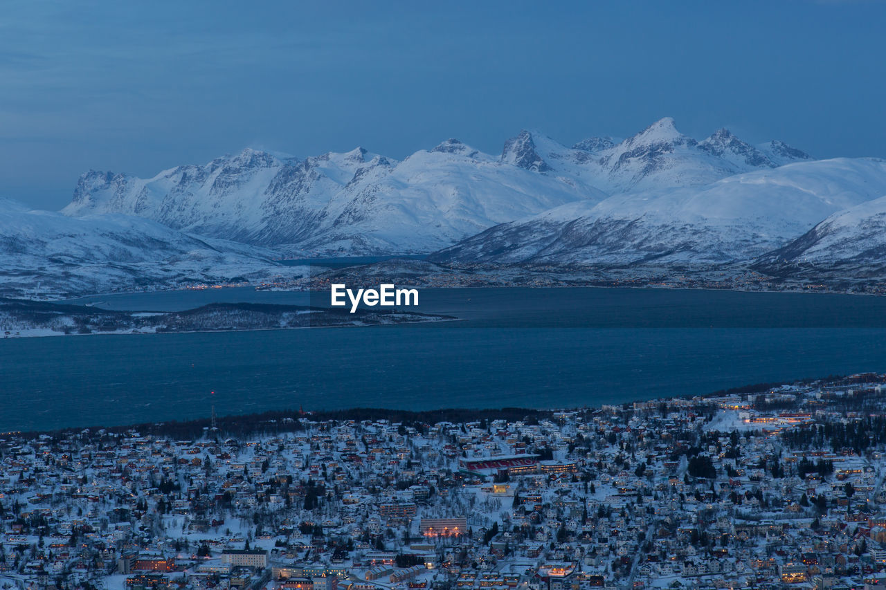 Town by fjord with snowcapped mountains against sky