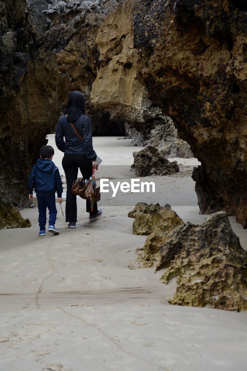 Mother and son walking through natural arch at beach