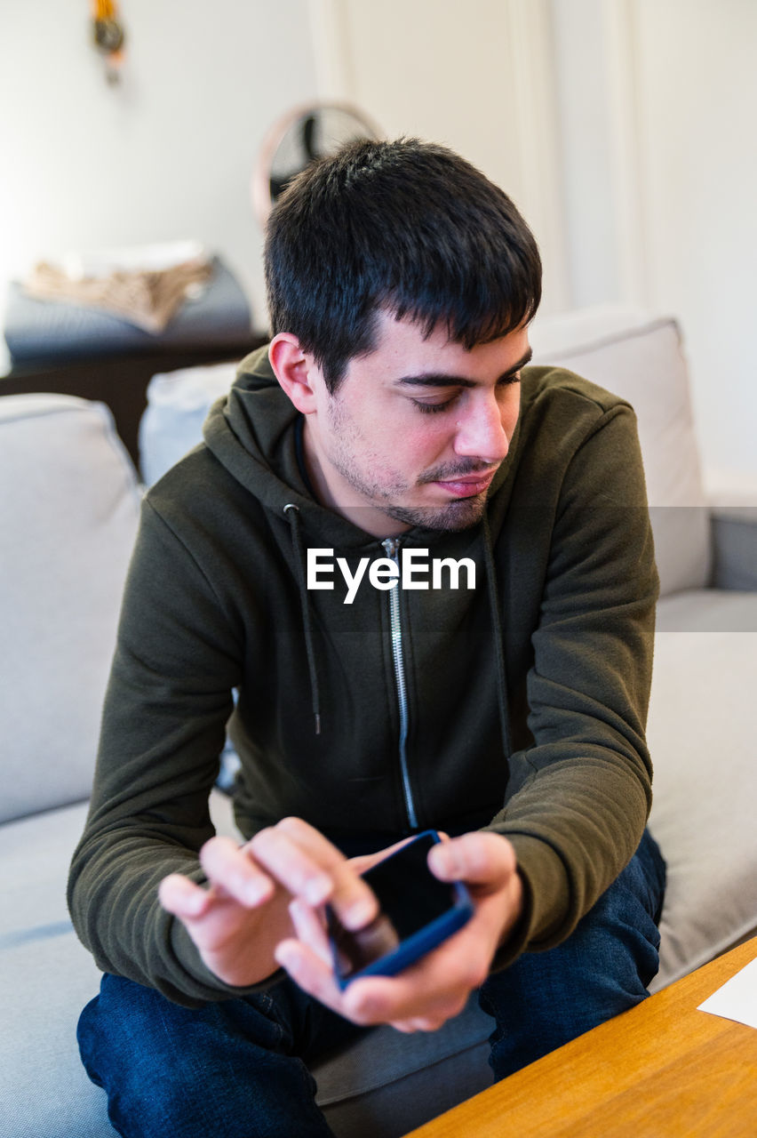 Male with eyesight disability scrolling mobile phone while sitting on couch at home