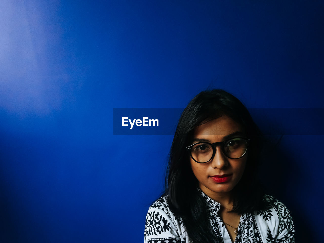 Close-up portrait of teenage girl wearing eyeglasses against blue wall