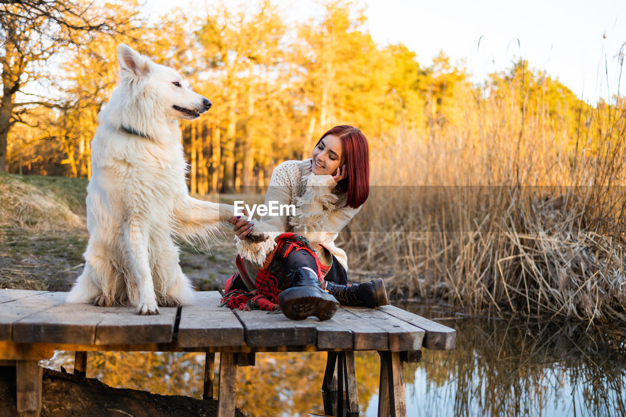 Woman relaxing with her samoyed dog on wooden bridge.