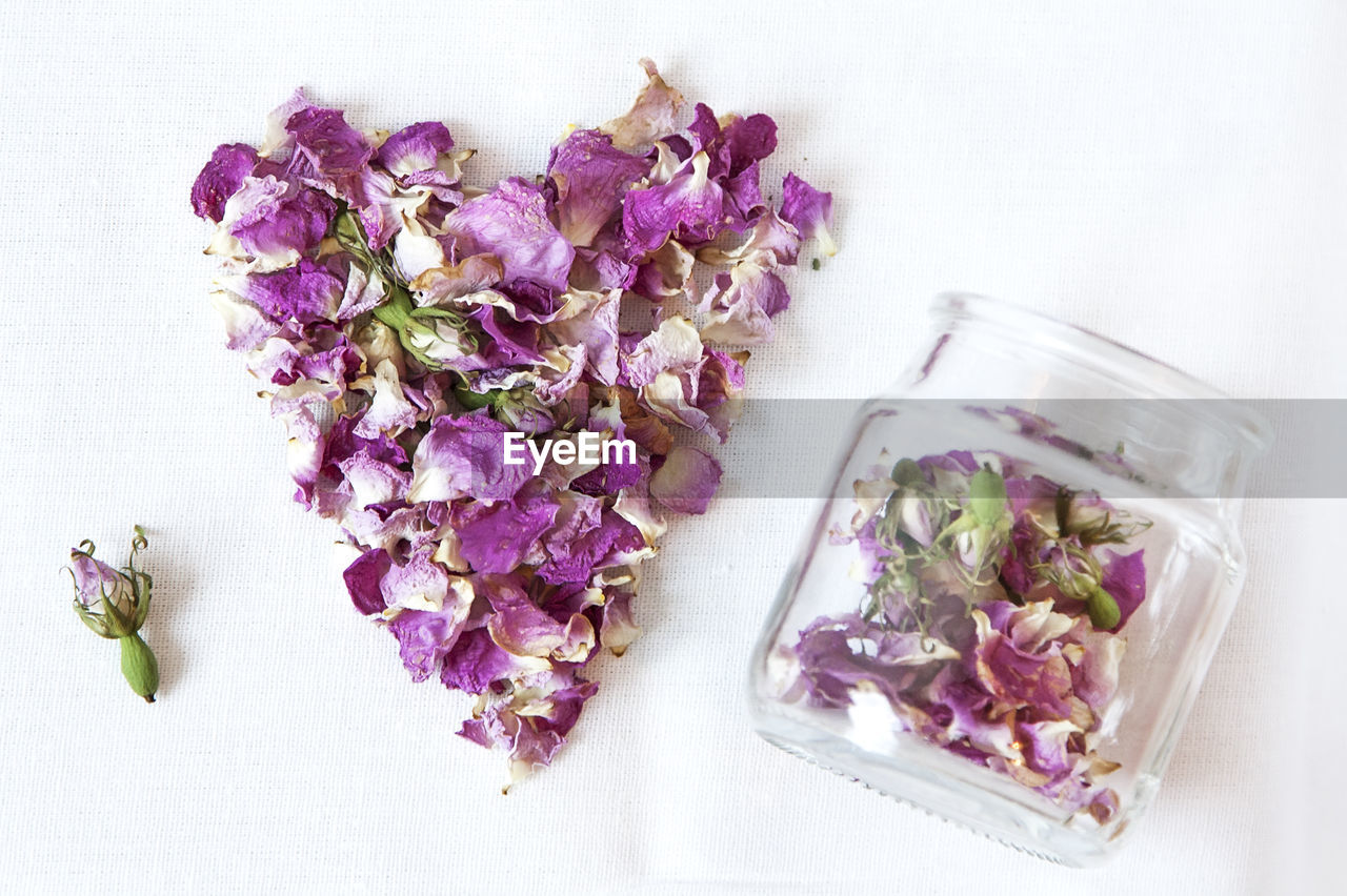 High angle view of rose hip petals in heart shape by jar on white background