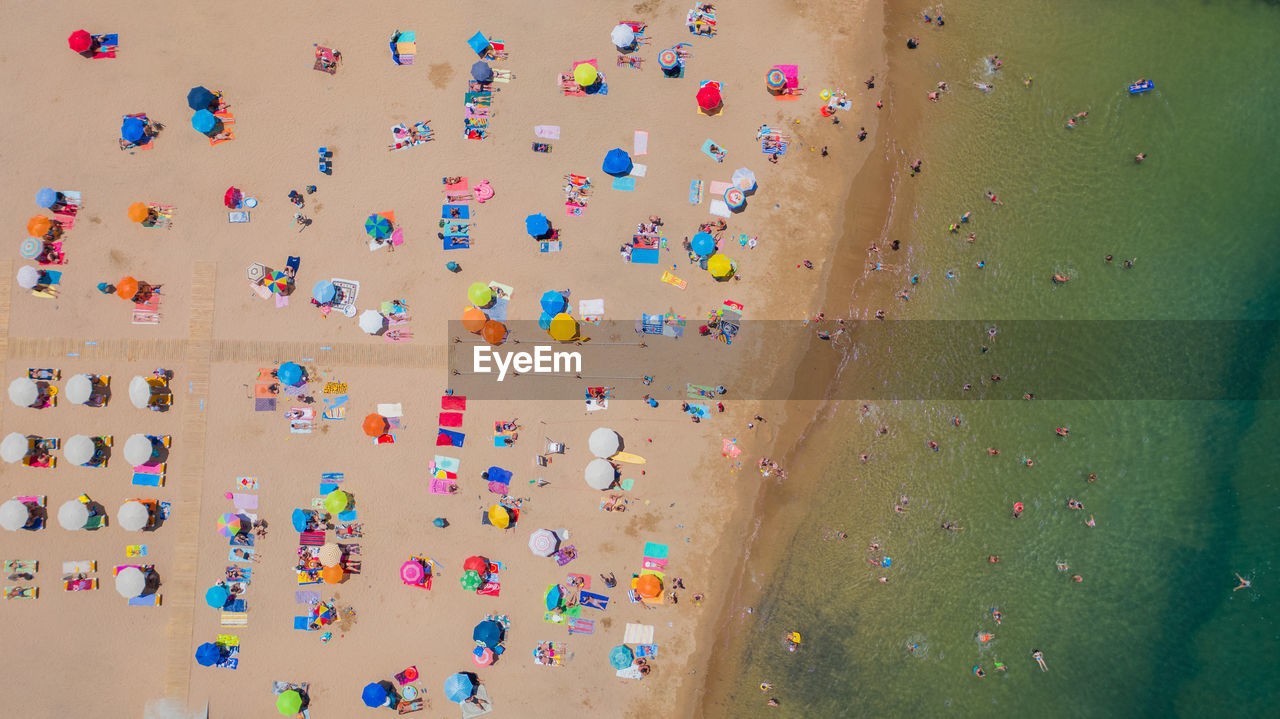 Aerial view of sandy beach with tourists swimming in beautiful clear sea water in madeira island.