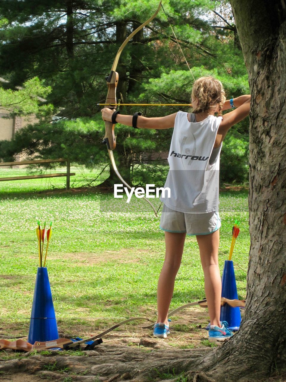 REAR VIEW OF YOUNG WOMAN STANDING ON TREE IN PARK