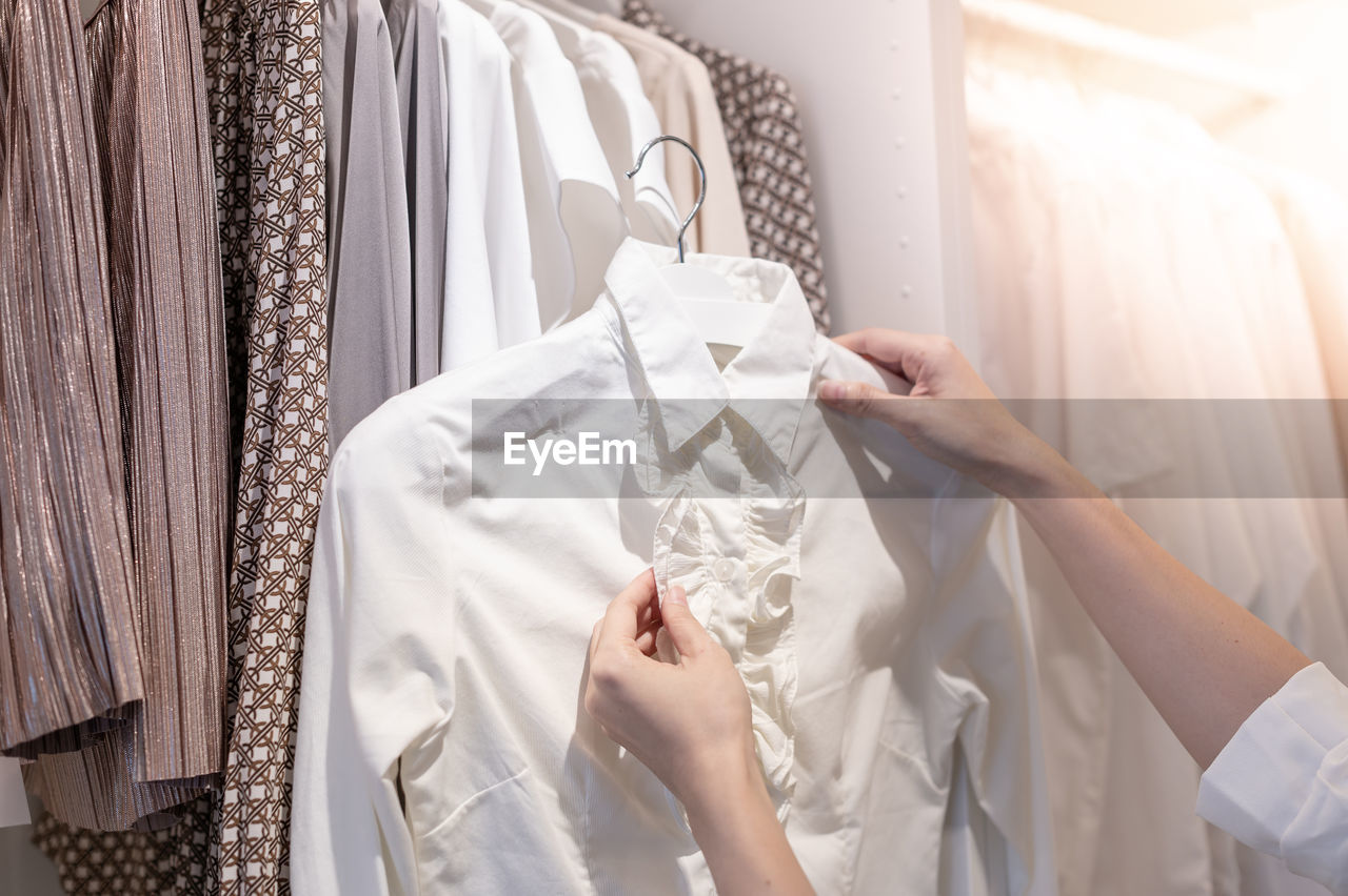 Female hand choosing clothes for checked pattern cotton polo shirt on the rack in cloth shop.