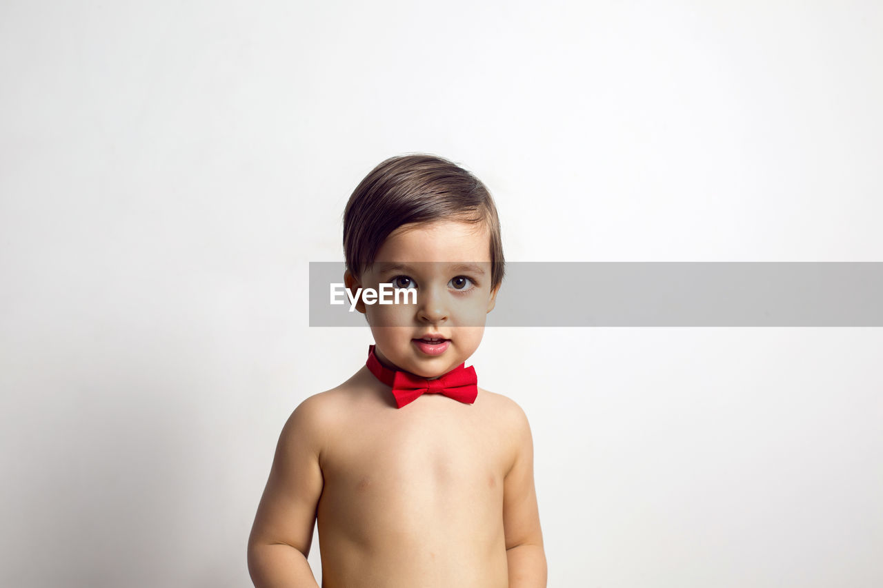 Child without a t-shirt sitting on a white background with a red bow tie