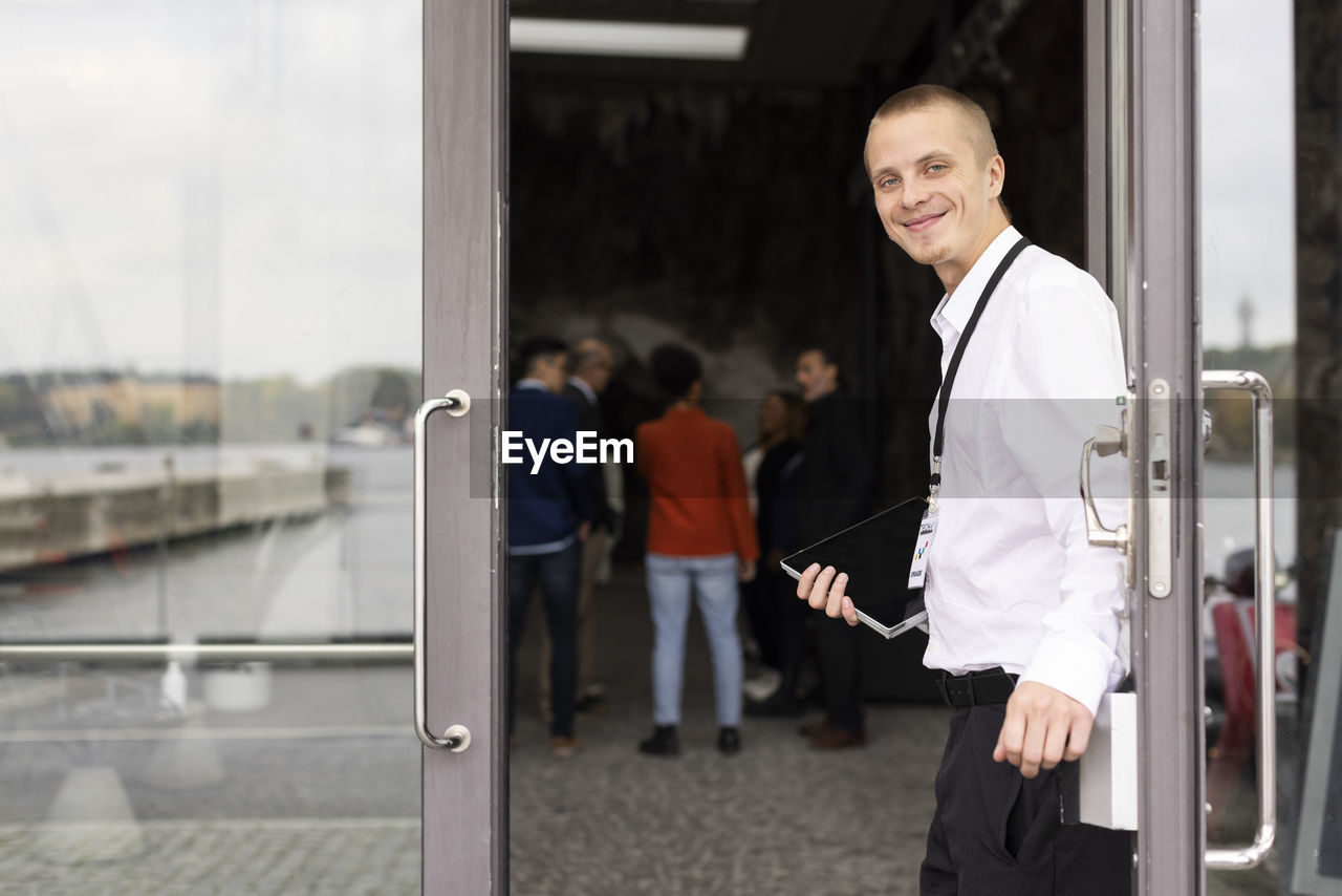 Portrait of smiling young businessman standing at doorway of convention center