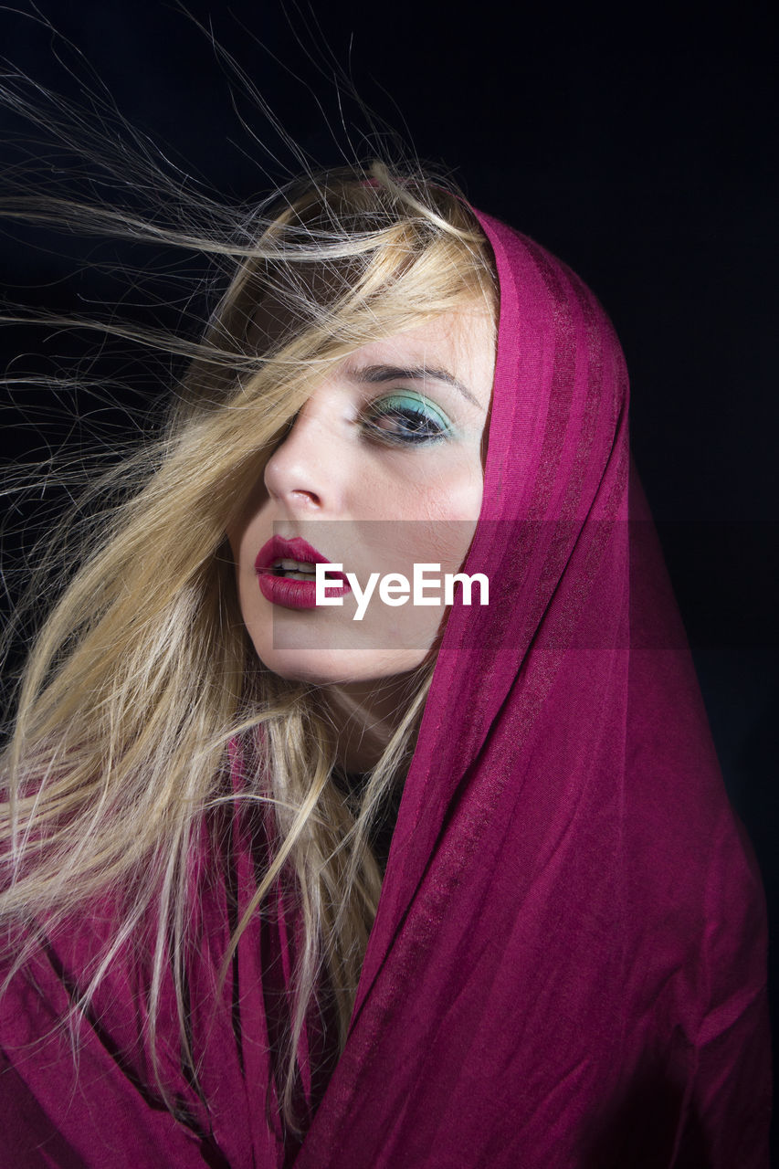 Close-up portrait of beautiful young woman over black background