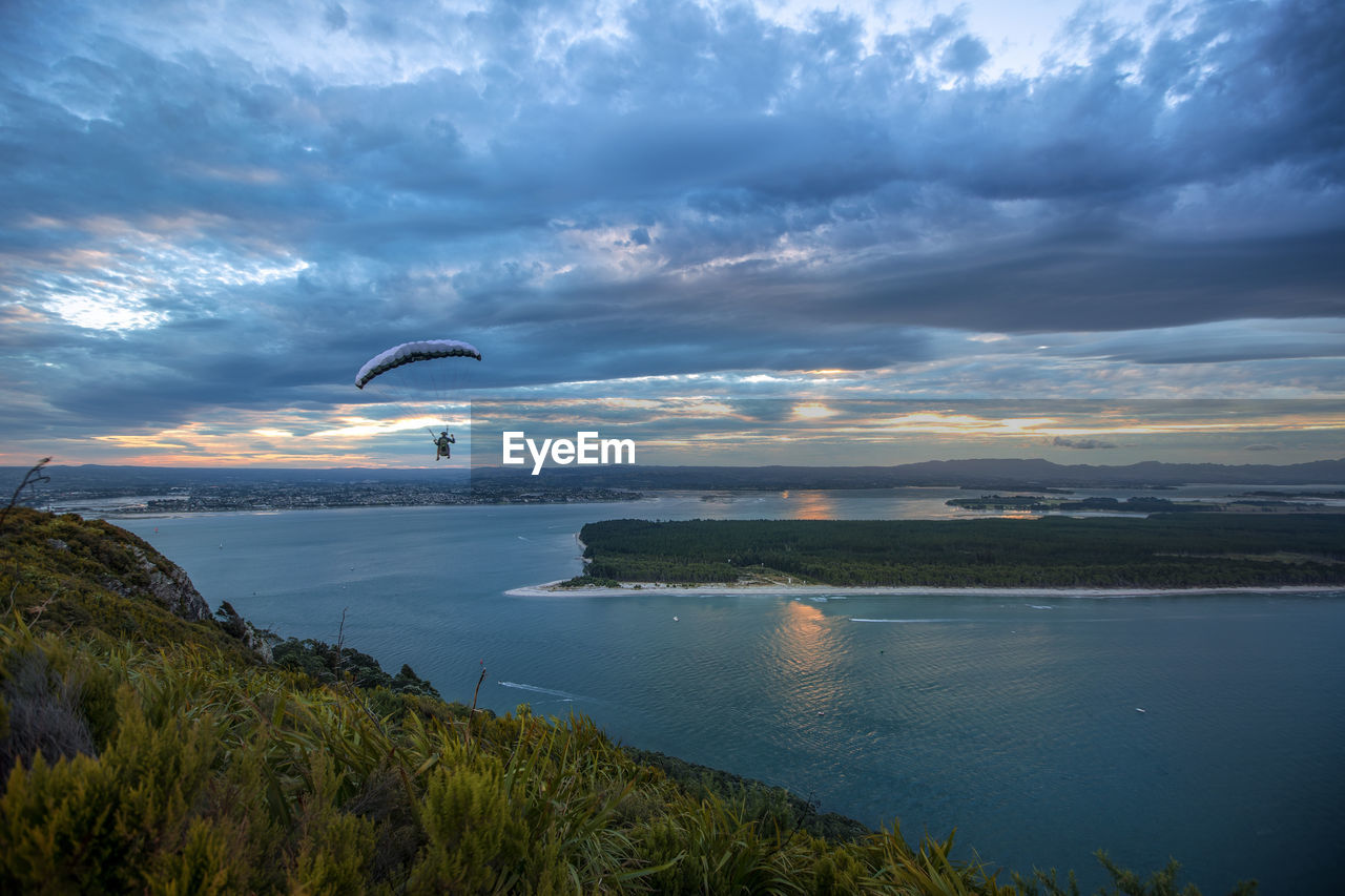 Person paragliding over sea against sky during sunset